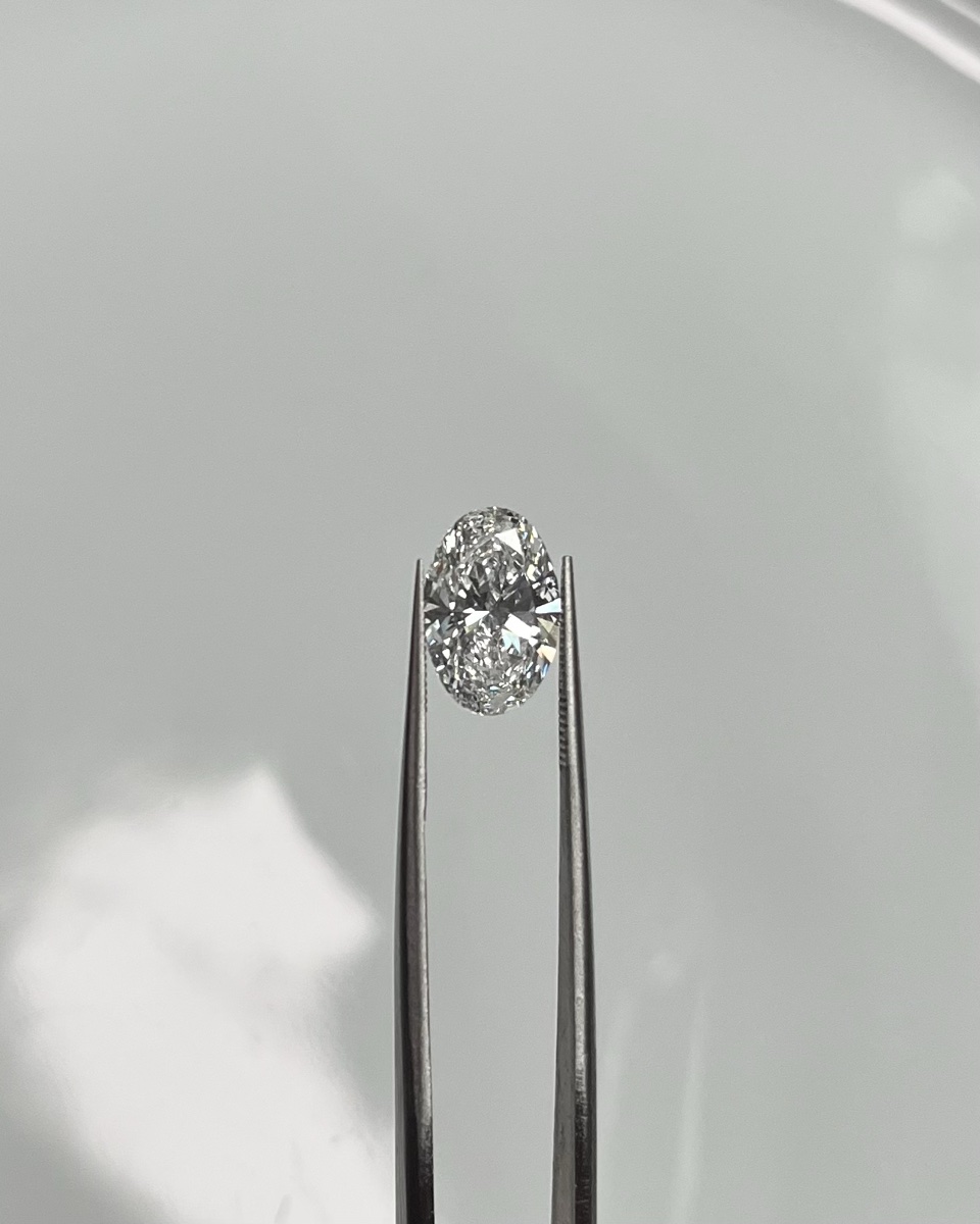 Macro photograph of a loose oval-cut diamond held with tweezers, showing its faceted brilliance